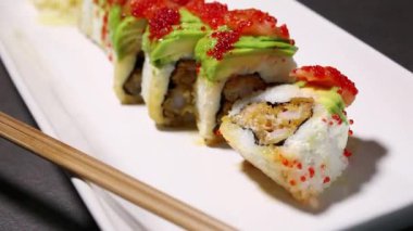 İçinde kızarmış karides ve beyaz tabağın üstünde taze avokado ve somon somonu olan suşi rulosunu kapat. 