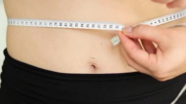 Karnını bant ile ölçen bir kadının yakın çekimi. Şişman, göbekli tiplerden. Sağlıksız yaşam tarzı diyet konsepti. Yüksek kaliteli FullHD görüntüler