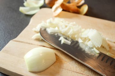 Tahta bir tahtanın üzerinde kesilmiş beyaz soğanı bıçakla kapat, koyu gri mutfak masası. 