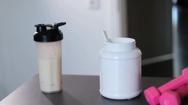 Bir kepçe protein tozu ve pembe dambıllar ve beyaz sümsük protein tozu ile dolu bir şişe yakın çekim yapın. Kilo kaybı için diyet yemeği.