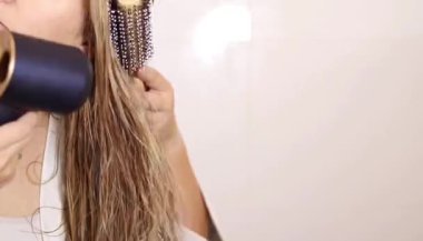 Sarışın saçlarını evde kurutan bir kadına yakın çekim. Ev konseptinde sağlıklı saç ve saç bakımı 