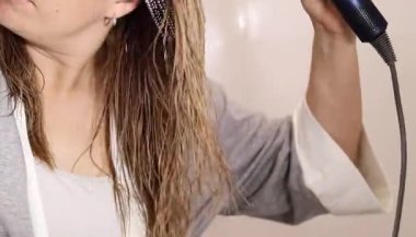 Sarışın saçlarını evde kurutan bir kadına yakın çekim. Ev konseptinde sağlıklı saç ve saç bakımı 