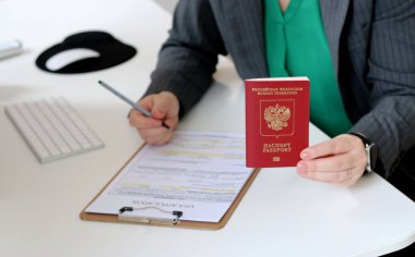 Beyaz bir kadının ofis masasında Rus pasaportu ile vize başvurusu formu doldurmasının üst görüntüsü.