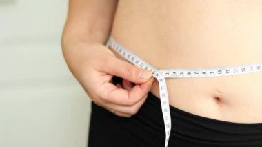 Karnını bant ile ölçen bir kadının yakın çekimi. Şişman, göbekli tiplerden. Sağlıksız yaşam tarzı diyet konsepti. Yüksek kaliteli FullHD görüntüler