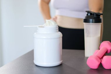 Mutfakta protein içeceği hazırlayan kadına yakın çekim. Kilo vermenin yerine diyet yemeği. Masada beyaz beyaz protein tozu ve pembe dambıllar var. 