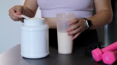 Mutfakta protein içeceği hazırlayan kadına yakın çekim. Kilo vermenin yerine diyet yemeği. Masada beyaz beyaz protein tozu ve pembe dambıllar var. 