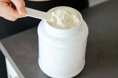Mutfakta protein içeceği hazırlayan kadının üst görüntüsü. Kilo vermenin yerine diyet yemeği. Bir kepçedeki beyaz süt proteini tozu 