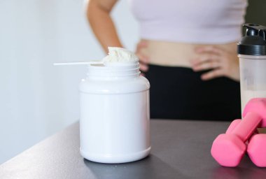Mutfakta protein içeceği hazırlayan kadına yakın çekim. Kilo vermenin yerine diyet yemeği. Masada beyaz beyaz protein tozu ve pembe dambıllar var. 