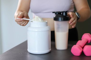 Mutfakta protein içeceği hazırlayan kadına yakın çekim. Kilo vermenin yerine diyet yemeği. Masada beyaz beyaz protein tozu ve pembe dambıllar var. 