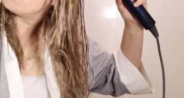 Sarışın saçlarını evde kurutan bir kadına yakın çekim. Ev konseptinde sağlıklı saç ve saç bakımı 