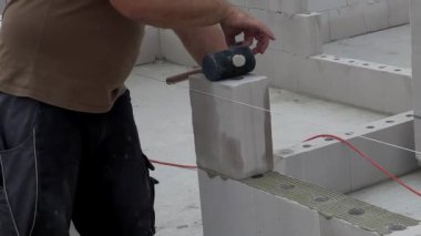 Duvarda beyaz taş ve beton yapıştırıcıyla duvar döşeyen bir inşaat işçisinin yakınına. Ev inşa etme kavramı 