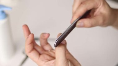 Evde tırnaklarını ojeleyen bir kadın, manikür yaptırıyor.