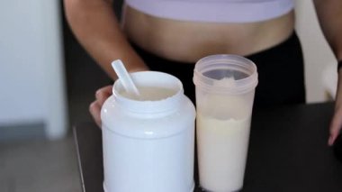 Mutfakta protein içeceği hazırlayan kadına yakın çekim. Kilo vermenin yerine diyet yemeği. Masada beyaz beyaz protein tozu ve pembe dambıllar var. 