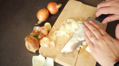 Kadın ellerinin ahşap tahtada çiğ beyaz soğan kesmesi, bulanık arka plan.