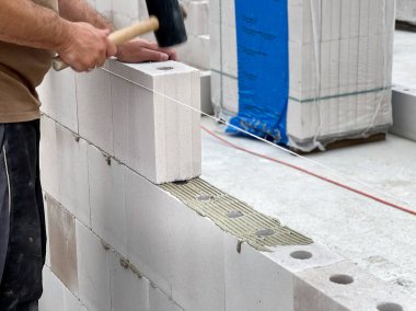 İnşaat işçisi beton kireç tuğlaları ve ince yatak yapıştırıcısıyla ev duvarları inşa ediyor. Almanya konseptinde inşaat alanı 