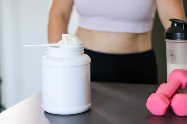 Mutfakta protein içeceği hazırlayan kadına yakın çekim. Kilo vermenin yerine diyet yemeği. Masada beyaz beyaz protein tozu ve pembe dambıllar var. 