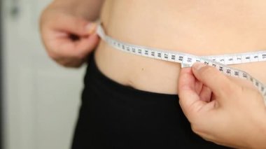Karnını bant ile ölçen bir kadının yakın çekimi. Şişman, göbekli tiplerden. Sağlıksız yaşam tarzı diyet konsepti. Yüksek kaliteli FullHD görüntüler