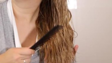 Islak sarı saçları siyah tarak, sağlıklı saç ve saç bakım konseptiyle tarayan bir kadın. Yüksek kaliteli FullHD görüntüler