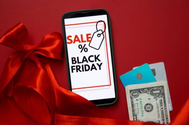 Kara Cuma online satışını kredi kartları ve parayla kırmızı arka planda gösteren bir akıllı telefon ekranının üst görüntüsü. Metin için boş kopyalama alanı