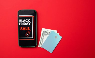 Kara Cuma online satışını kredi kartları ve parayla kırmızı arka planda gösteren bir akıllı telefon ekranının üst görüntüsü. Metin için ücretsiz kopyalama alanı olan pankart