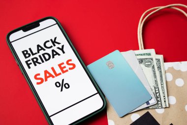 Kara Cuma online satışını kredi kartları, nakit para ve bir alışveriş çantası ile kırmızı arka planda gösteren akıllı telefon ekranının üst görüntüsünü kapat