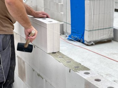 İnşaat işçisi beton kireç tuğlaları ve ince yatak yapıştırıcısıyla ev duvarları inşa ediyor. Almanya konseptinde inşaat alanı 