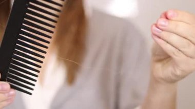 Sarışın bir kadının saçını tarağın üzerinde bulmasını yakından çek. Saç dökülmesi konsepti. Beyaz bulanık arka plan duvarı. Yüksek kaliteli FullHD görüntüler