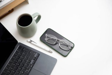 Şeffaf bardakları, dizüstü bilgisayarı, kahve fincanı ve beyaz masadaki malzemeleri olan bir iş yeri. Minimalist ve modern ofis ya da İçişleri Bakanlığı konsepti 