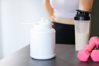 Mutfakta protein içeceği hazırlayan kadına yakın çekim. Kilo vermenin yerine diyet yemeği. Masada beyaz beyaz protein tozu ve pembe dambıllar var. 