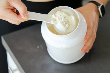 Mutfakta protein içeceği hazırlayan kadının üst görüntüsü. Kilo vermenin yerine diyet yemeği. Bir kepçedeki beyaz süt proteini tozu 