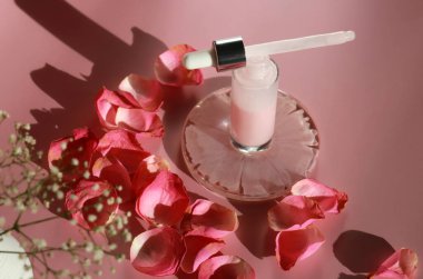 Pembe arka planda ve pembe yapraklarda gül özü olan bir şişe yüz serumu losyonu. Nemlendirici cilt bakımı ürün konseptini oluşturur