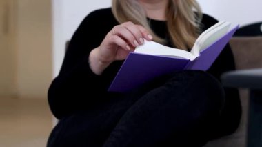 Kafkasyalı bir kadının kanepede oturduğu ve mor bir maket kitap okuduğu, arka planda bulanıklık olan 