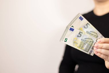 Beş avroluk banknotlar tutan bir kadının elini kapat. Para, kopya alanı olan gri bir arkaplan. 
