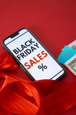 Kara Cuma online satışını kredi kartları ve parayla kırmızı arka planda gösteren bir akıllı telefon ekranının üst görüntüsü. Metin için boş kopyalama alanı