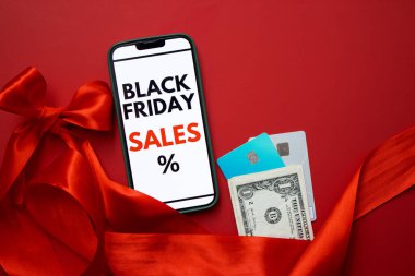 Kara Cuma online satışını kredi kartları ve parayla kırmızı arka planda gösteren bir akıllı telefon ekranının üst görüntüsü. Metin için boş kopyalama alanı