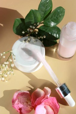 Bej arka planı, yeşil yaprakları ve yaprakları olan bir şişe yüz serumu losyonunu kapat. Nemlendirici cilt bakımı ürün konseptini oluşturur