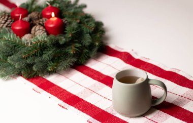 Beyaz masada kırmızı mumlar ve çelenklerle dolu sıcak bir bardak. Konforlu ev dekorasyonu 