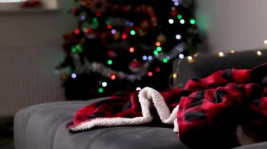 Gri bir kanepedeki kırmızı battaniyeyi kapat. Arka plan bulanık ve Noel ağacı ışıkları var. Tatillerde rahat ve şenlikli bir ev