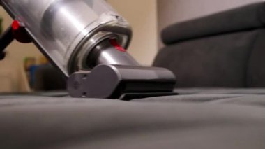 Oturma odasında elektrikli süpürgeyle gri bir kanepeyi temizleyen kadın elini kapat. 