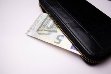 Siyah deri cüzdan ve beyaz masa arkasında beş euro banknotlar.