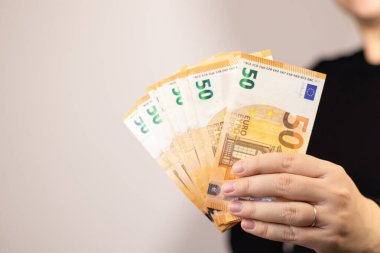 Elli euro banknot tutan bir kadının yakın plan fotoğrafı. Fotokopi alanı olan gri arka plan.