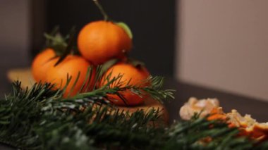 Soyulmuş mandalinayı ve ahşap tabakta bir yığın mandalinayı, önündeki bulanık yeşil çam dalını, gri masa arkasını kapatın. Yüksek kaliteli FullHD görüntüler