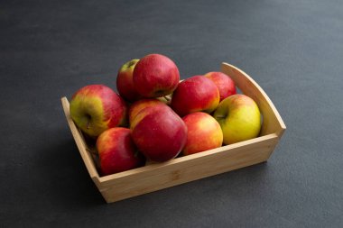 Koyu gri masa arkaplanındaki ahşap sandıkta taze, küçük organik kırmızı elmalar.