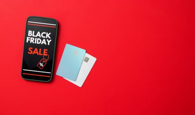 Kara Cuma online satışını kredi kartlarıyla kırmızı arka planda gösteren bir akıllı telefon ekranının üst görüntüsü. Metin için ücretsiz kopyalama alanı olan pankart