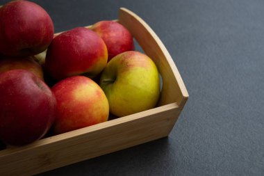 Koyu gri masa arkaplanındaki ahşap sandıkta taze, küçük organik kırmızı elmalar.