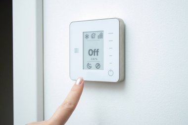 Beyaz duvardaki modern termostat kontrol sistemine dokunan kadın parmağını kapat. Ev konseptinde klima 