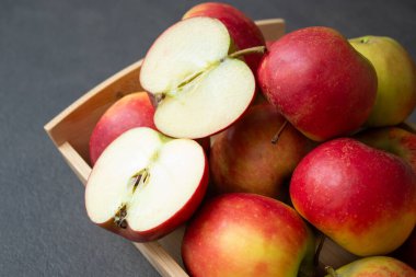 Koyu gri masa arkaplanındaki ahşap sandıkta taze, küçük organik kırmızı elmalar.