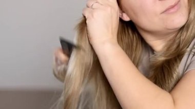 Beyaz bir kadının, sarı saçlarını siyah bir tarakla tarayan portresini yakından çek. Yüksek kaliteli FullHD görüntüler