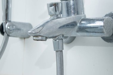 Kireçtaşı lekeli, beyaz karolar duvarlı bir küvetin musluğunu kapat.