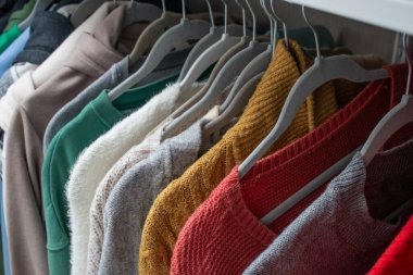 Kadın sonbaharını ve kışları dolaptaki askıların üzerine sıcak örülmüş kumaşları kapatın. Rahat ve renkli kostüm konsepti